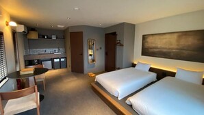 Een hotelkamer met twee bedden, een bureau, een stoel, een kleine kitchenette en een spiegel.