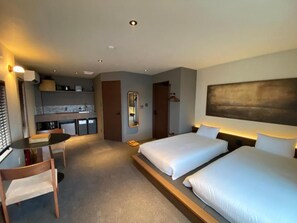 A hotel room with two beds, a desk, a chair, a small kitchenette, and a mirror. - HITOYOI SENRI Rooftop BBQ Ocean View (Fukuoka)