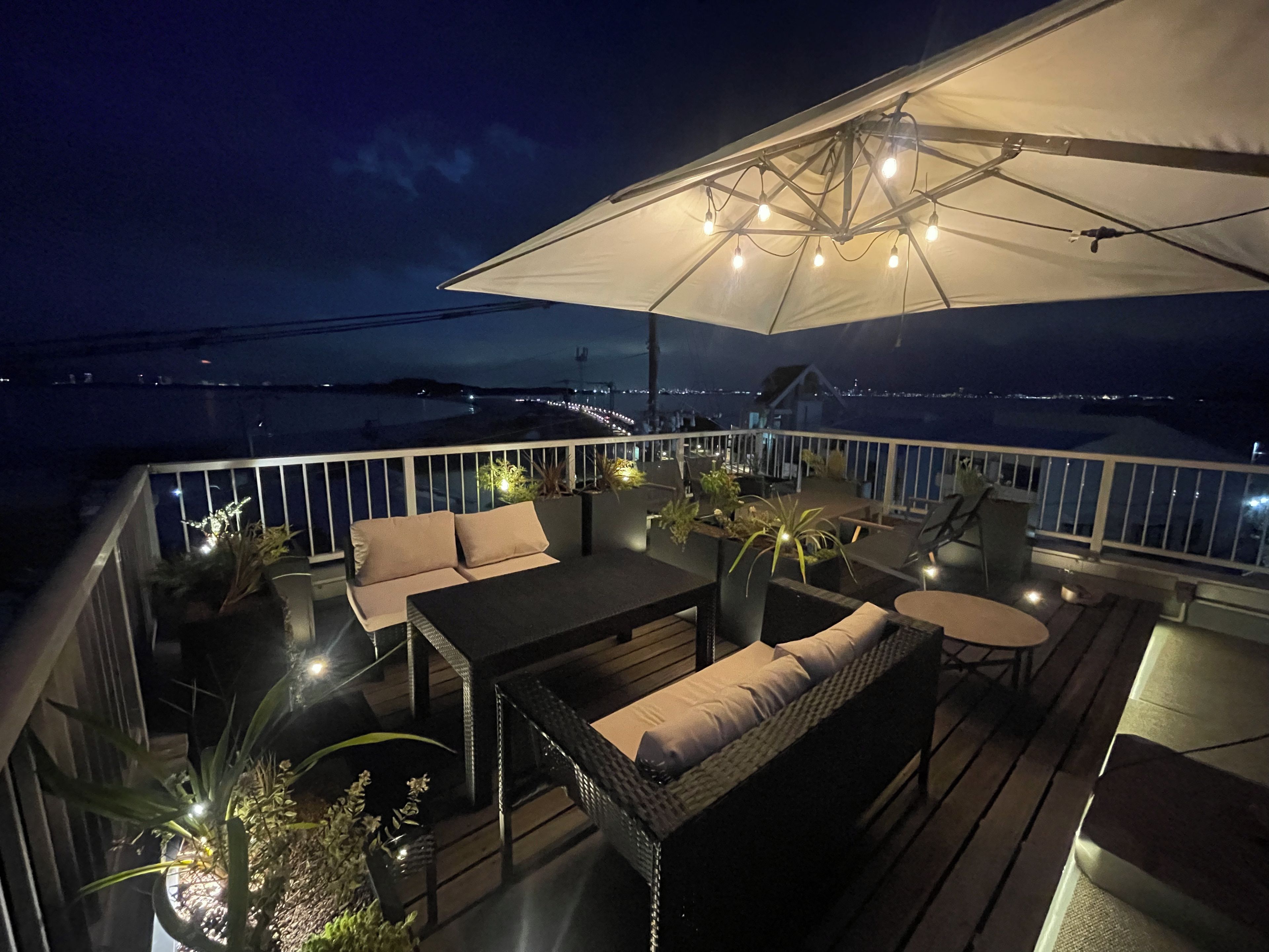 A deck with outdoor furniture, a large umbrella, and a view of the water.