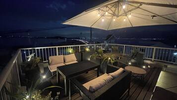 A deck with outdoor furniture, a large umbrella, and a view of the water.
