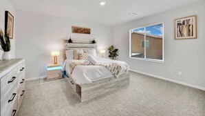 Quarto com cama, mesas de cabeceira, cômoda e janela com persianas.