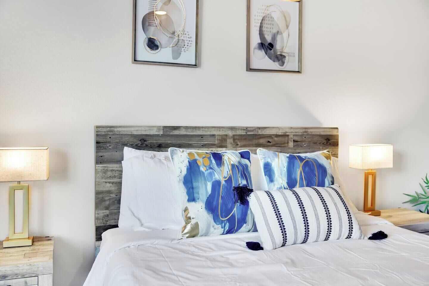 Un lit bien fait, avec une literie blanche et des coussins décoratifs, une tête de lit en bois et deux lampes de chevet posées sur des tables de nuit en bois.