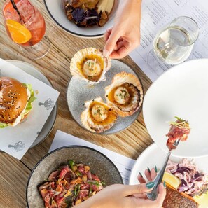 A dining table with various dishes, including a burger, scallops, and a salad. - The Avenue - Brand New Luxury, Walk to Main Street (Mornington)