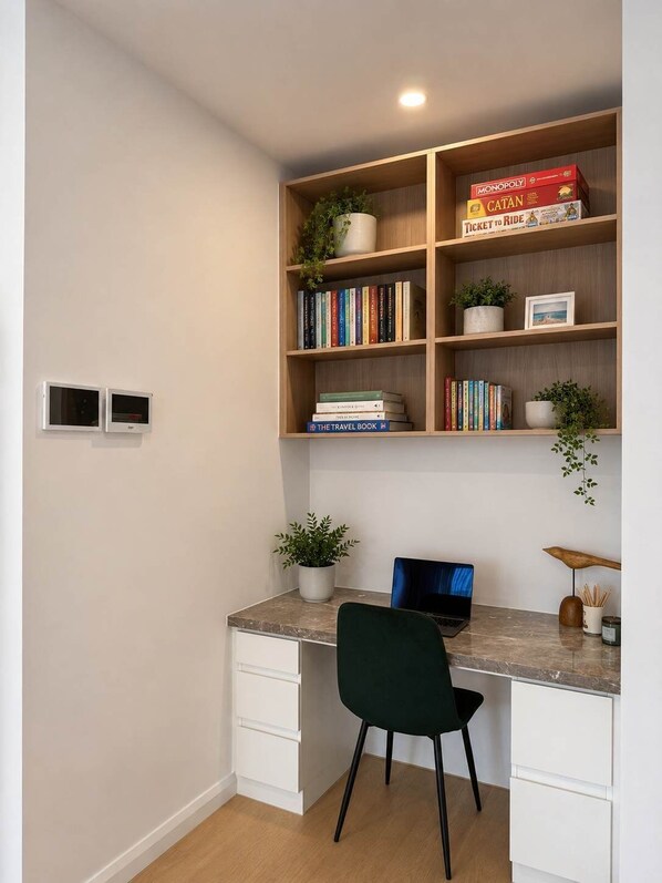 Un salón de estudio con escritorio, silla, estanterías y una planta pequeña.