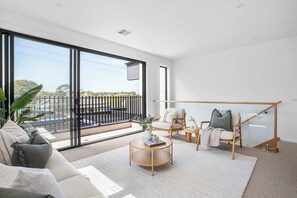 A modern living room with a large sliding glass door leading to a balcony, a sofa set, a coffee table, and a wooden chair. - The Avenue - Brand New Luxury, Walk to Main Street (Mornington)