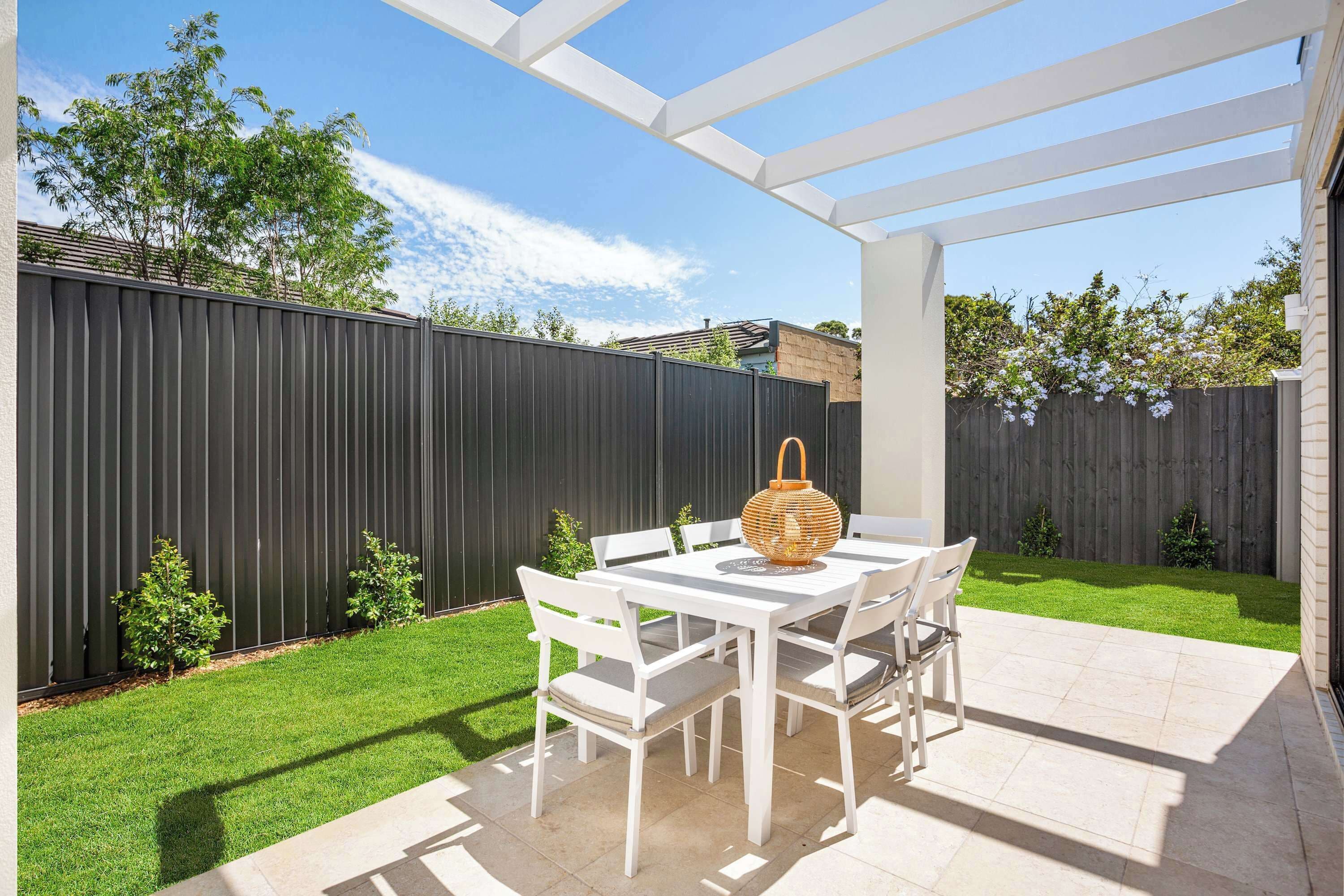 A patio area with a white table and chairs, a woven basket, and a black fence.