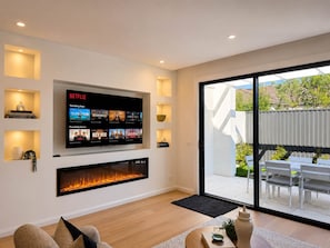 Una sala de estar moderna con un televisor de pantalla plana montado en la pared, una chimenea debajo y una puerta corrediza de vidrio que da a un patio exterior.