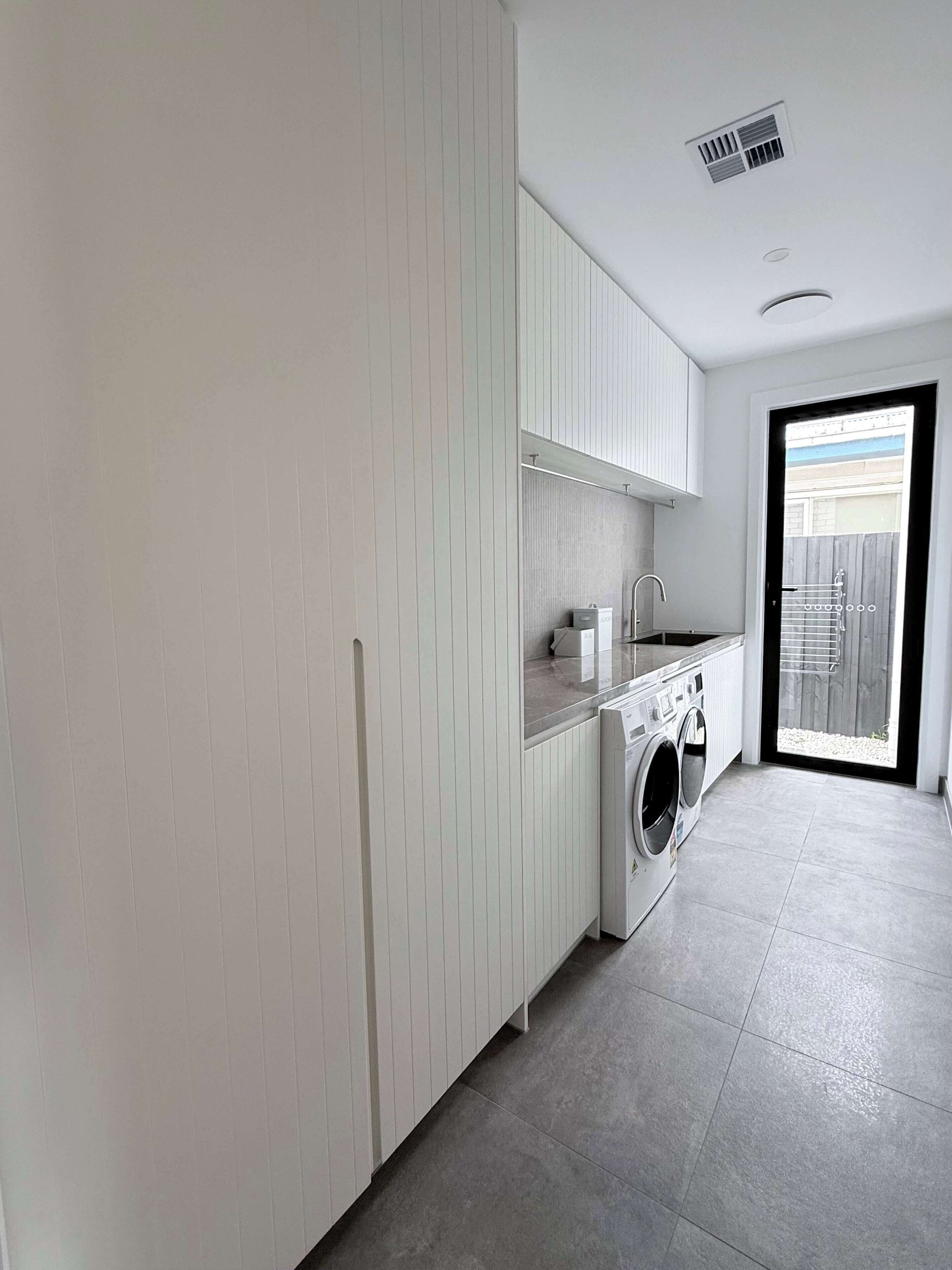Een moderne keuken met een inbouw wasmachine, een spoelbak en een raam met uitzicht op een achtertuin.