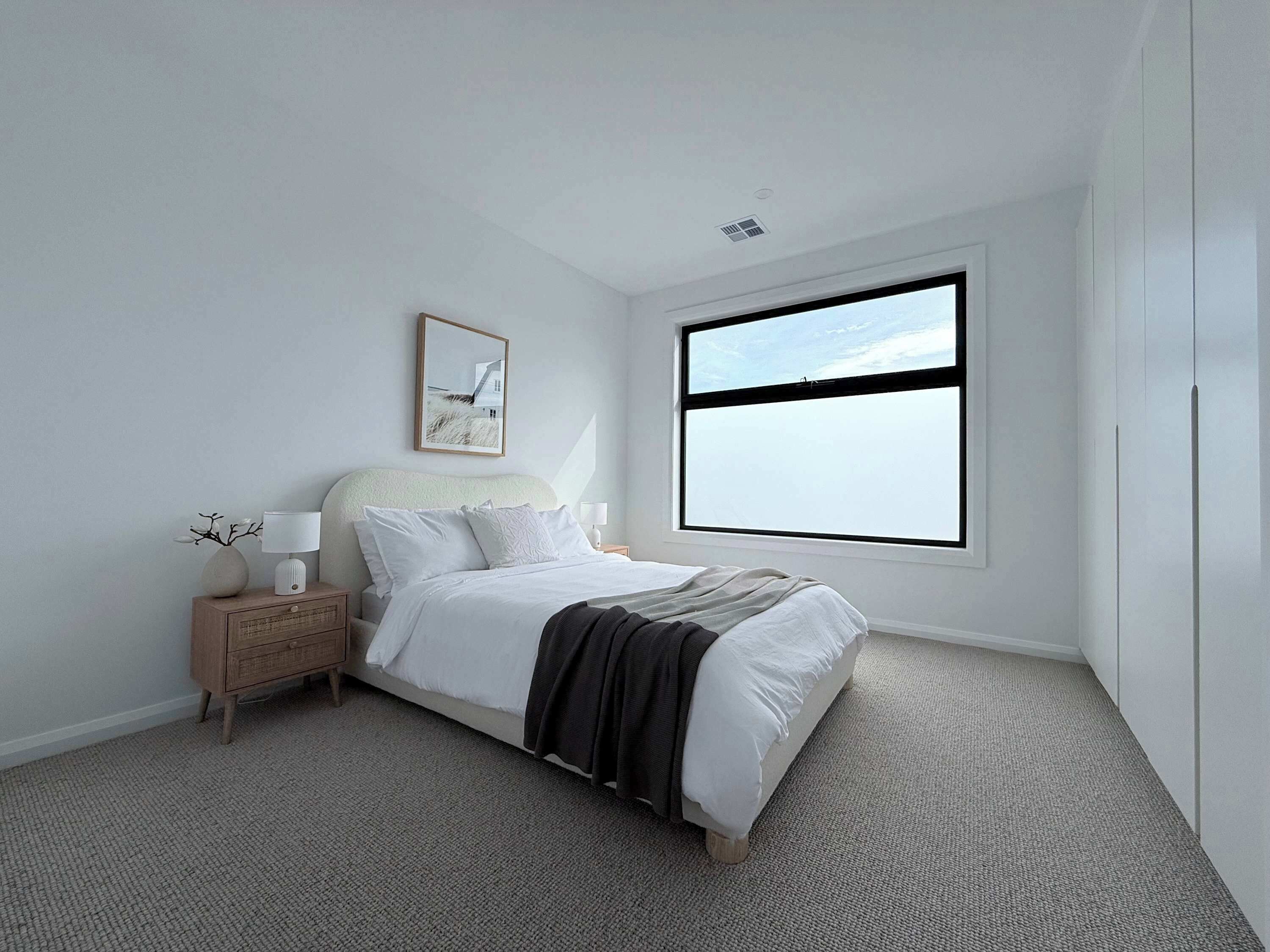 A minimalist bedroom with a large window, a bedside table with a lamp, and a framed picture on the wall.