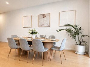 A dining area with a round table, grey upholstered chairs, and a potted plant. - The Avenue - Brand New Luxury, Walk to Main Street (Mornington)