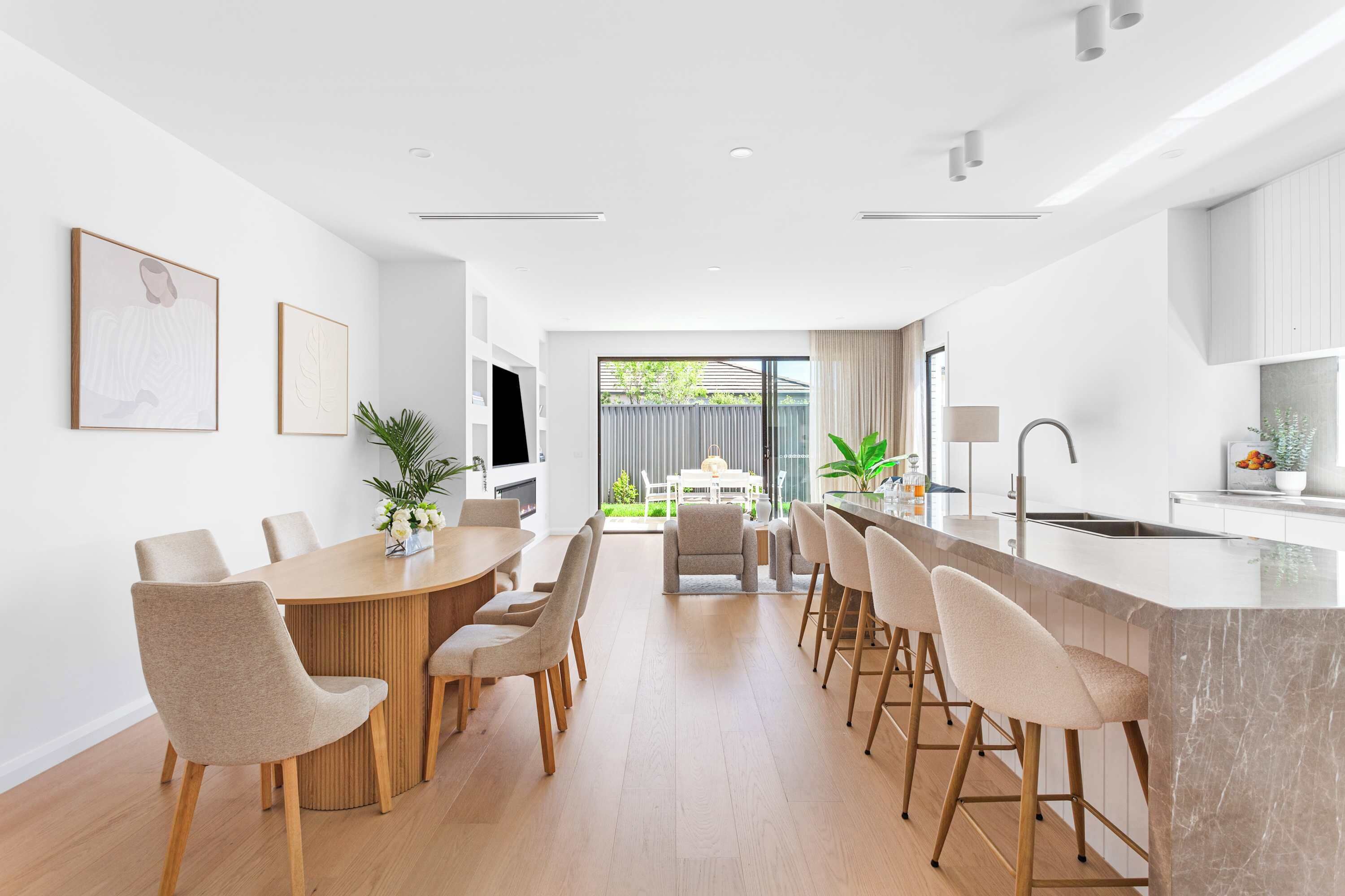 Een moderne keuken met een eethoek, met een houten eettafel, barstoelen en een groot raam.