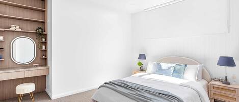 A bedroom with a bed, bedside tables, a dresser, a mirror, and a small stool.