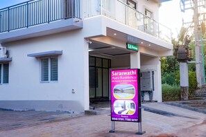 Un edificio con un cartel anunciando Auro Residency, que muestra números de contacto e imágenes de habitaciones y piscinas.