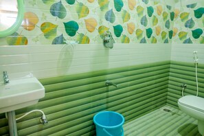 A bathroom with a green and white tiled wall, a sink, a toilet, and a blue bucket. - Saraswathi Auro Residency (Vanur)
