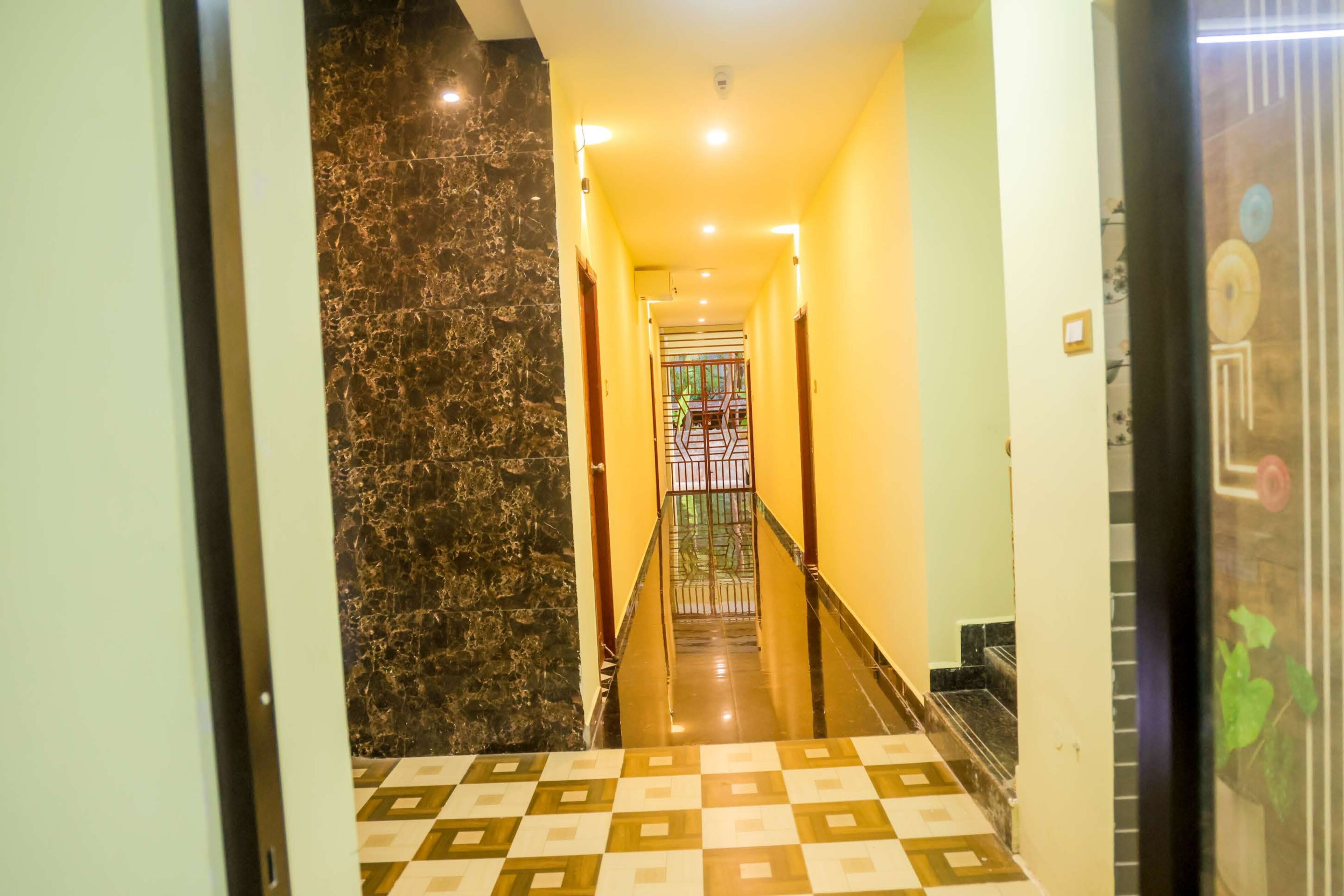 Corredor de hotel com parede de mármore, piso quadriculado e portão no final.