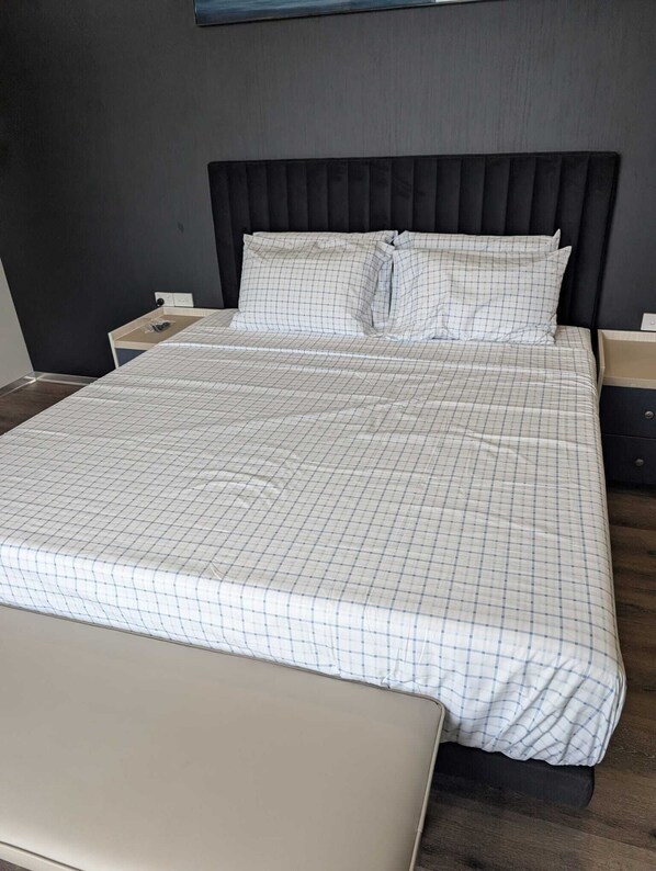 A bed with a checkered bedspread and two pillows, a bedside table, and a nightstand.