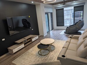 A modern living room with a flat-screen TV, a gaming chair, a sofa, and a coffee table.