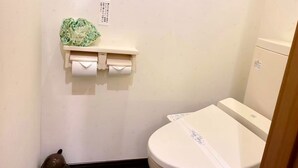 A small bathroom with a toilet, a shelf with toilet paper, and a decorative item on the wall. - Hanatsuki・Kakure Onsen Resort Villa Hotel (Izu Kogen) (伊東市)
