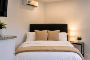 Ein Hotelzimmer mit einem Bett, einem Nachttisch, einer Lampe und einer Klimaanlage.