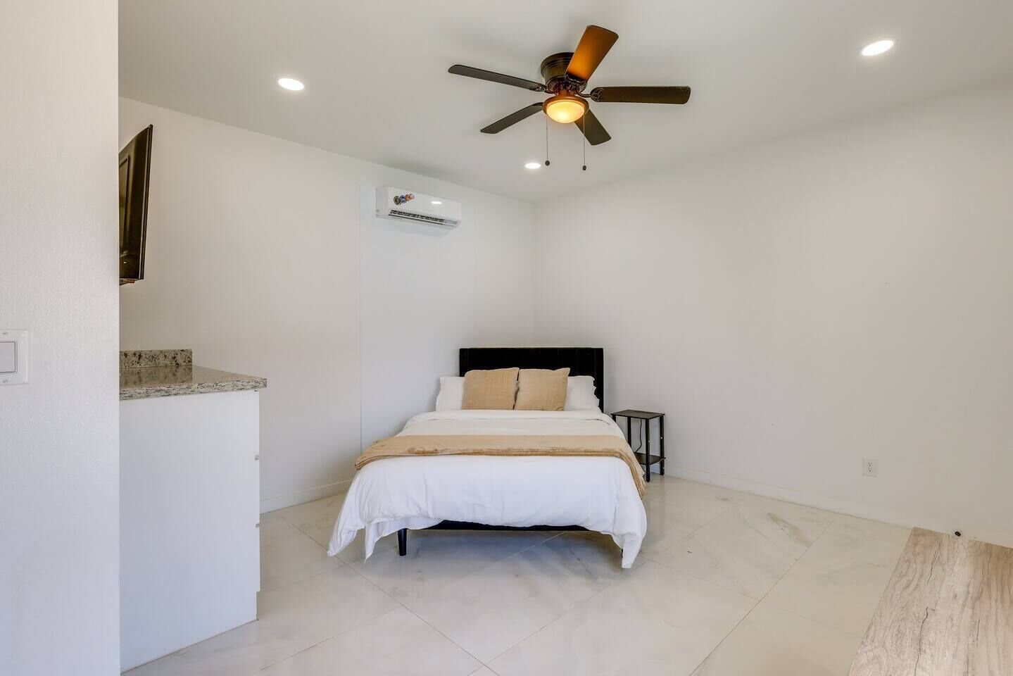Un dormitorio con cama, ventilador de techo, unidad de aire acondicionado y una mesita de noche.