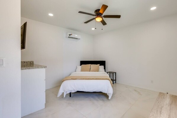 Un dormitorio con cama, ventilador de techo, unidad de aire acondicionado y una mesita de noche.