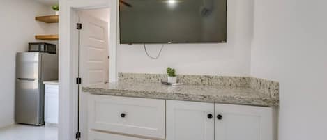A kitchen with white cabinets, a granite countertop, a stainless steel refrigerator, a microwave, and a flat-screen TV mounted above the counter.