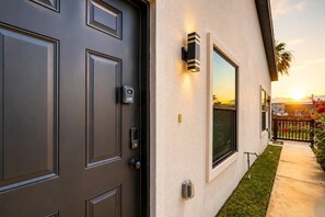 A modern house exterior with a dark grey door, a keypad lock, and a wall-mounted light fixture.