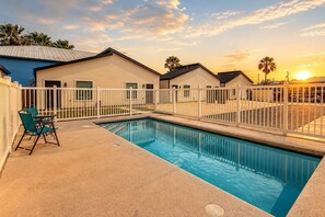 A swimming pool with a white fence, a chair, and a building with a flat roof.
