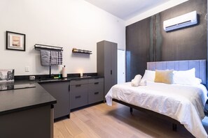 A modern hotel room with a bed, a small kitchenette, a dark-colored wardrobe, and a wall-mounted air conditioner. - Spruce Villa - 2nd Floor Queen Studio (Philadelphia)