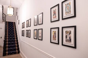 Een gang met kunstwerken in lijsten aan de muur en een trap met een kamerbreed tapijt.