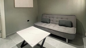 Uma sala de estar moderna com um sofá cinza, uma mesa de centro branca e piso de azulejos.