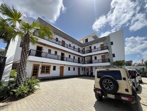 A multi-story building with balconies, a paved driveway, and a parked SUV.