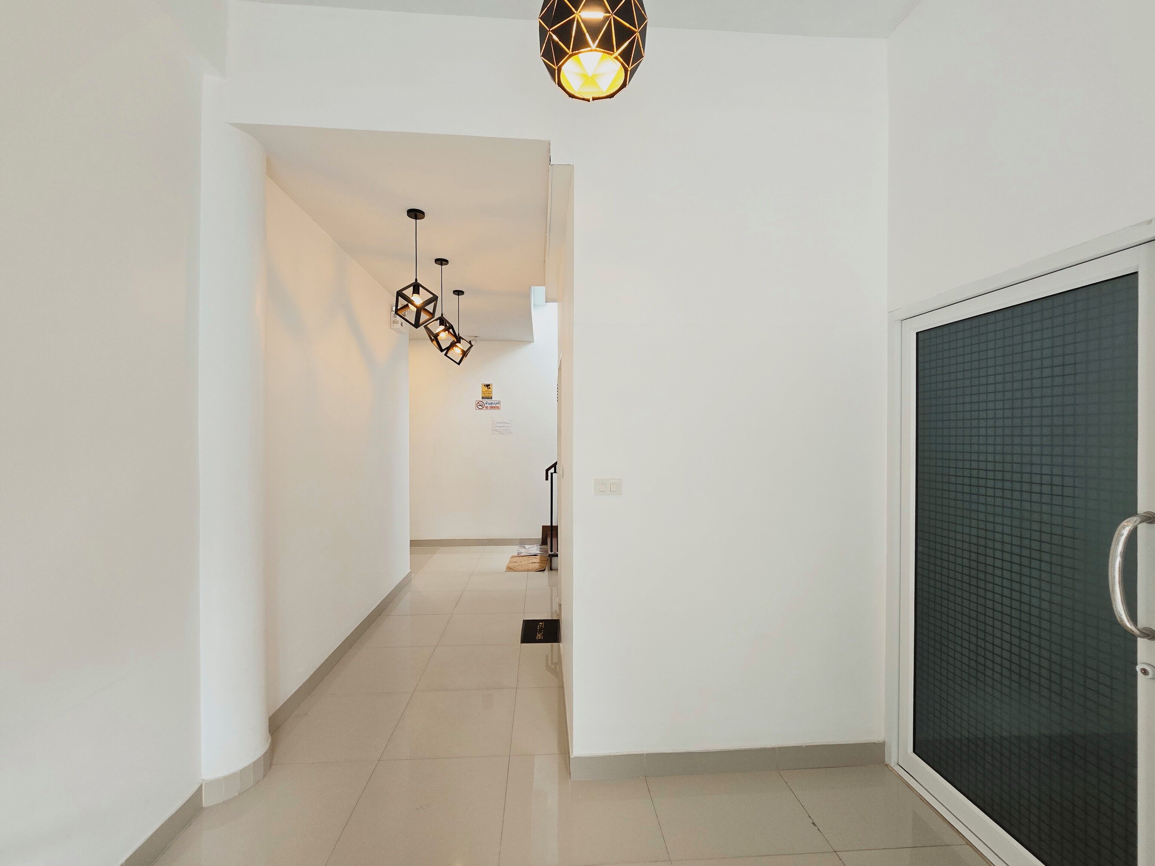 A hallway with a modern light fixture, a door with a metal handle, and a tiled floor.