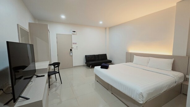 A hotel room with a bed, a desk with a chair, a television, and a door.