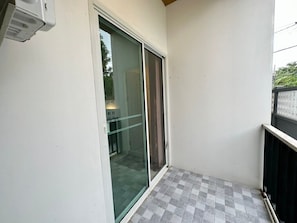 A small balcony with a glass door leading to a room, a checkered floor, and a white wall. - Hada House near Yanhee Hospital (Bangkok)