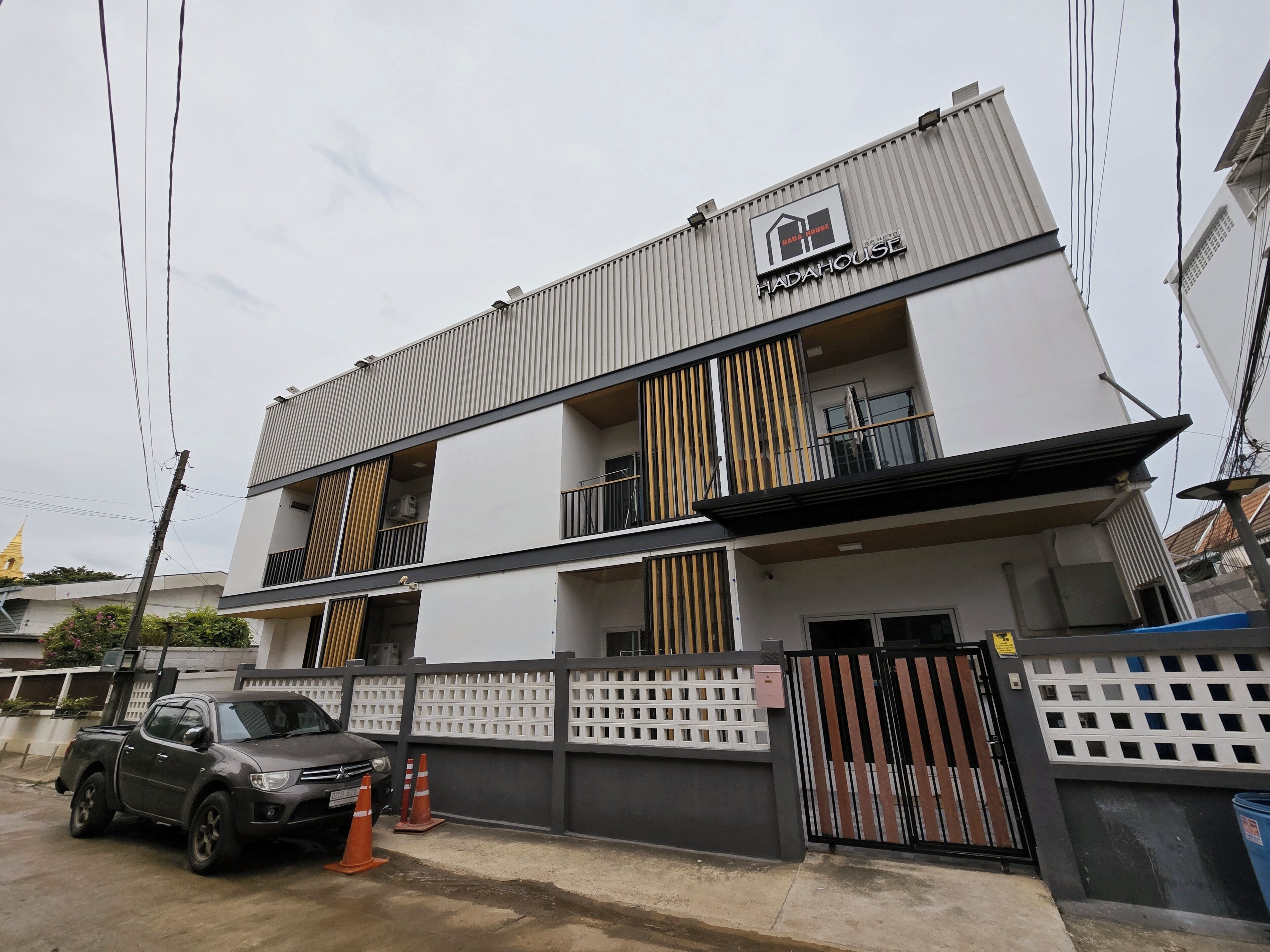 Un edificio moderno de dos pisos con entrada protegida por un portón, un balcón visible y un vehículo estacionado.