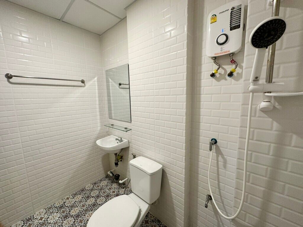 Ett badrum med vita kakelbeklädda väggar, en toalett, ett handfat och en dusch med ett duschmunstycke som kan hållas i handen.