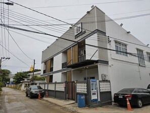 A two-story building with a gated entrance, a blue trash bin, and a parked car.