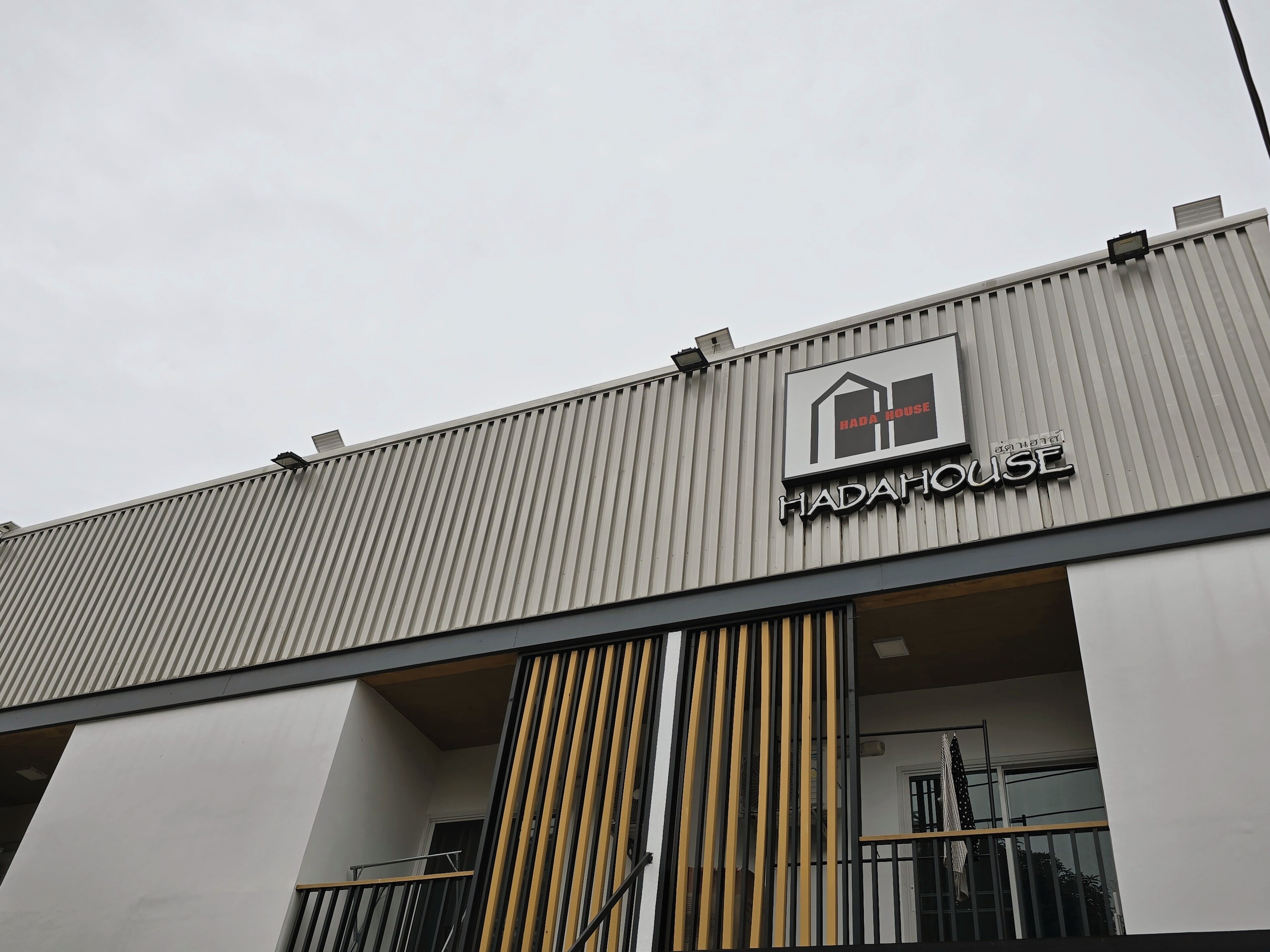 A building with a modern facade, a sign reading 'HADA HOUSE', and a large entrance with vertical blinds.