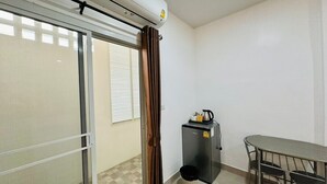 A room with a sliding glass door, a small kitchenette with a refrigerator, a table, and a chair.