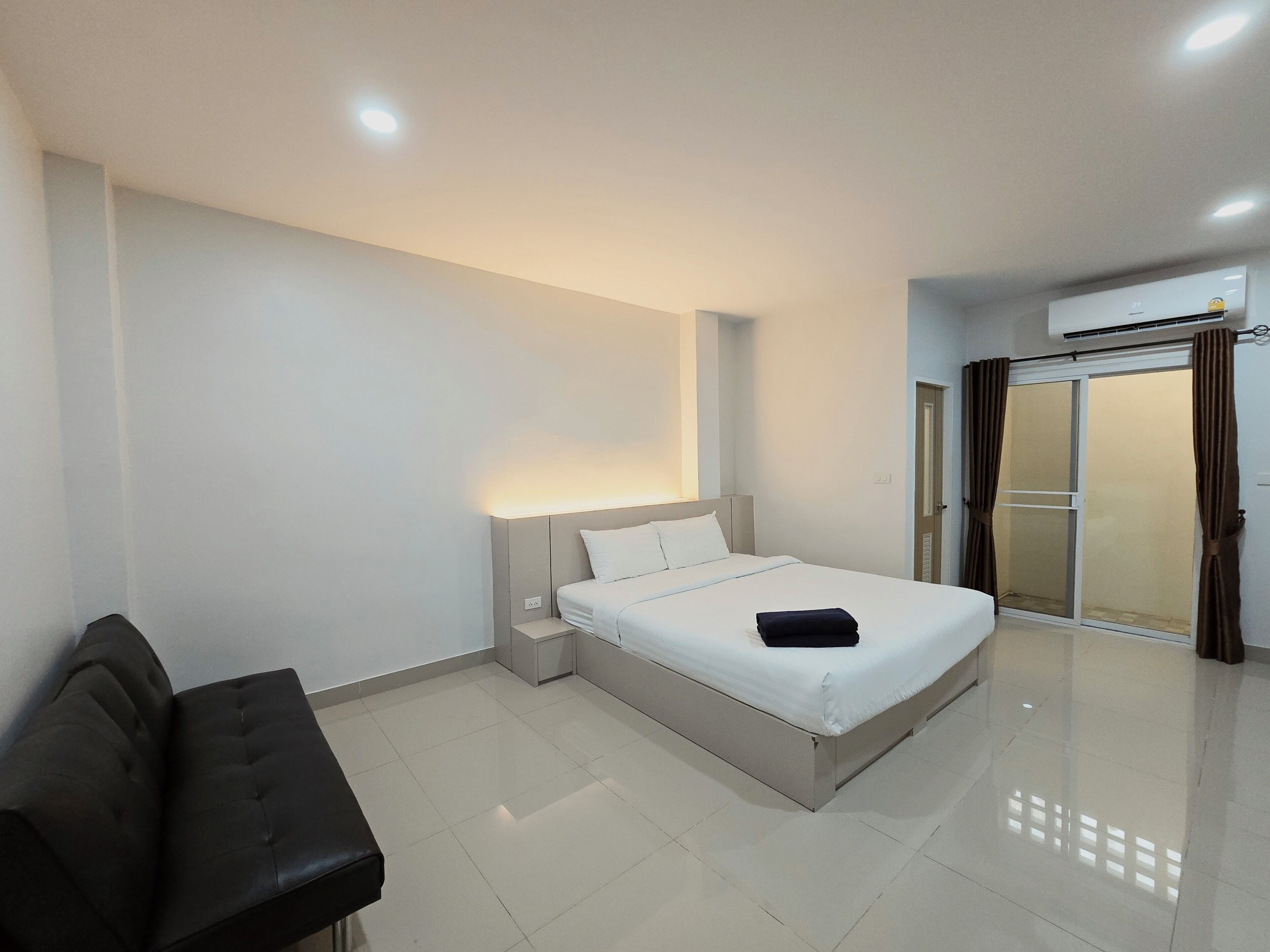 Une chambre d’hôtel moderne, équipée d’un lit, d’une table de chevet, d’une chaise et d’une porte-fenêtre coulissante donnant sur un balcon.