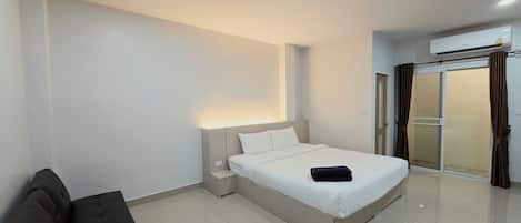 A modern hotel room with a bed, a bedside table, a chair, and a sliding glass door leading to a balcony.