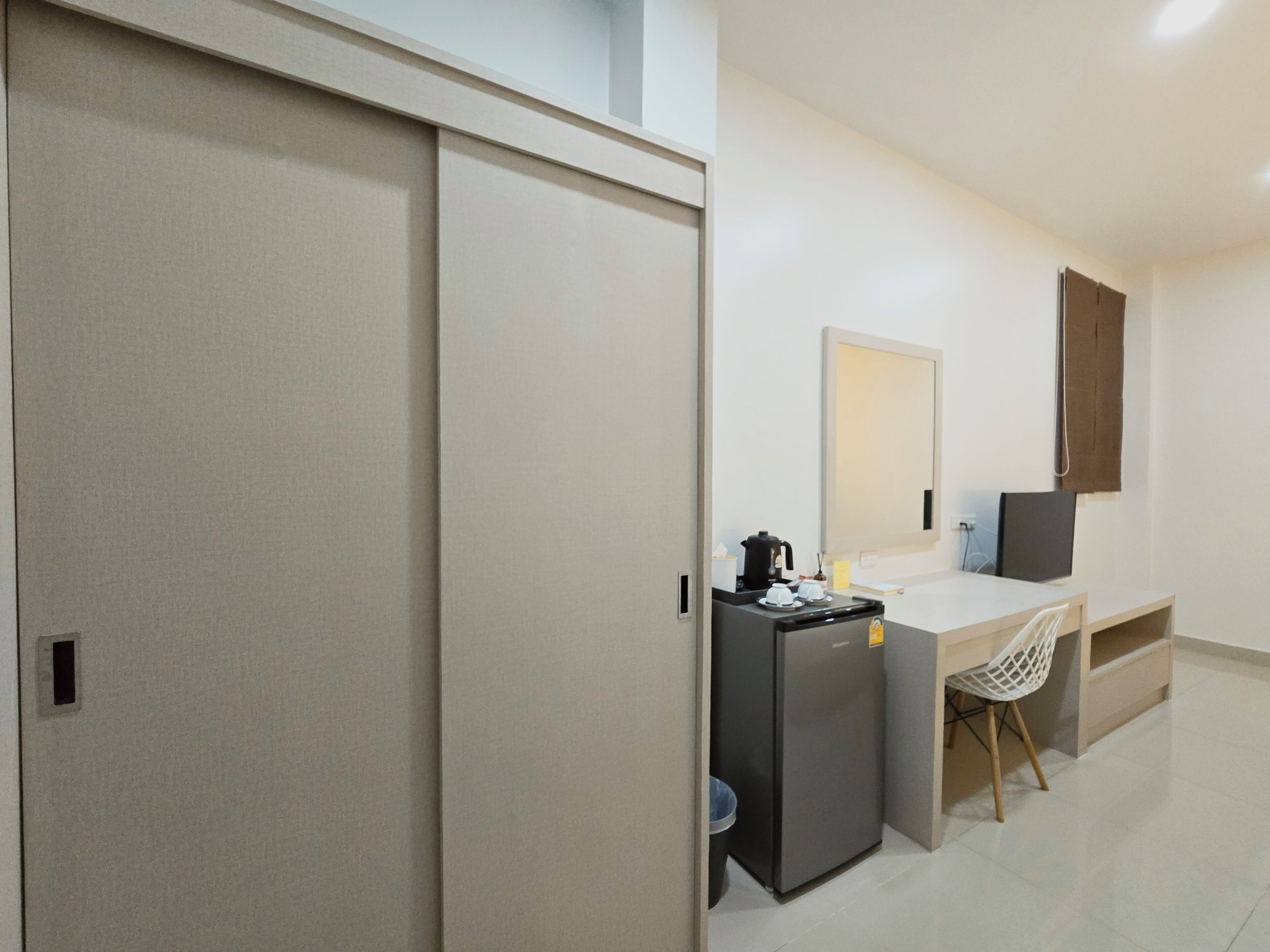 Een kleine hotelkamer met kitchenette, bureau, stoel en grote spiegel.
