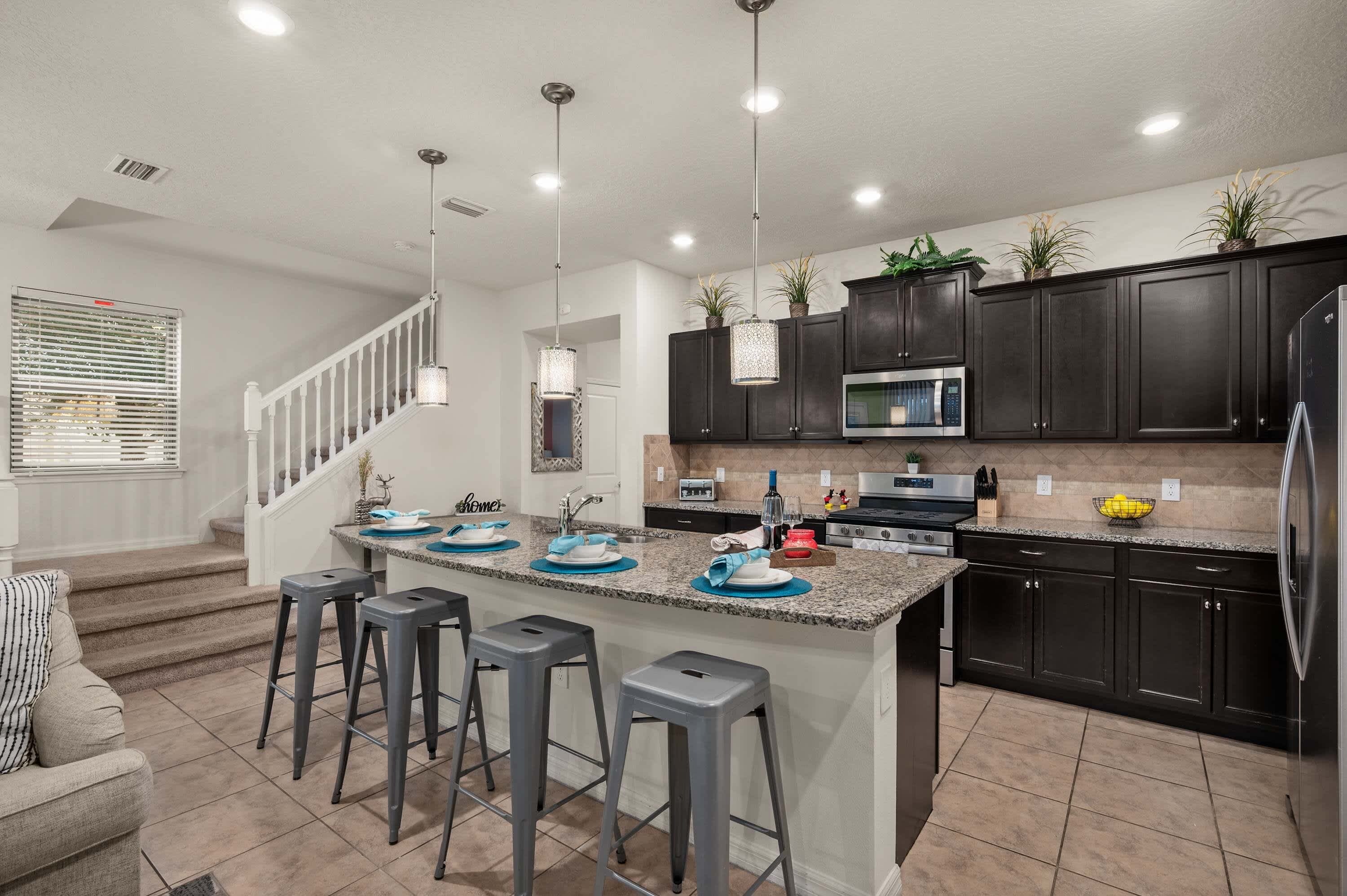 A modern kitchen with a central island, bar stools, dark cabinets, stainless steel appliances, and pendant lighting.