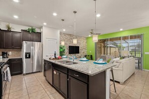 A modern kitchen with a central island, stainless steel appliances, and a dining area with a sofa and table. - 5BR Solterra Escape w/ Private Pool & Themes (Davenport)