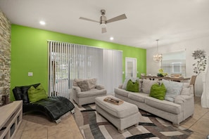 A living room with a green accent wall, a ceiling fan, a dining area with a table and chairs, and a decorative plant. - 5BR Solterra Escape w/ Private Pool & Themes (Davenport)