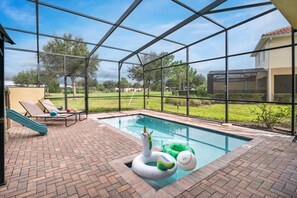 Piscina com escorregador e espreguiçadeiras, cercada por um ambiente envidraçado com vista para uma área residencial.