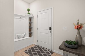 A hallway with a white door, a welcome sign, a shelf with letters spelling 'HOME,' a cushion with a nautical theme, and a small table with a vase and plants. - 5BR Solterra Escape w/ Private Pool & Themes (Davenport)