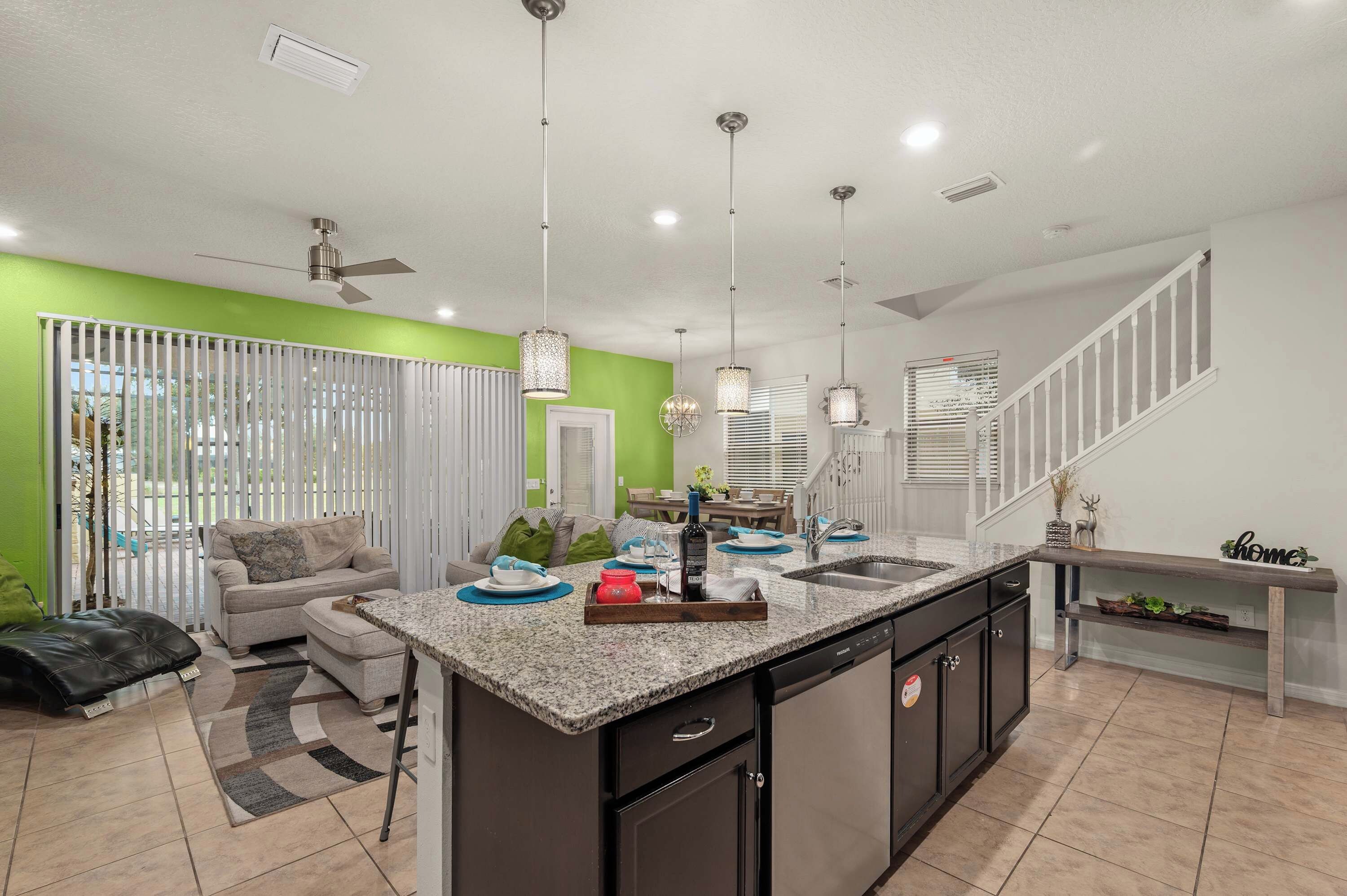 A modern kitchen with a central island, a dining area with a sofa, and a staircase.