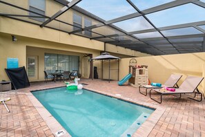 An indoor swimming pool with a slide, lounge chairs, and a covered patio area. - 5BR Solterra Escape w/ Private Pool & Themes (Davenport)